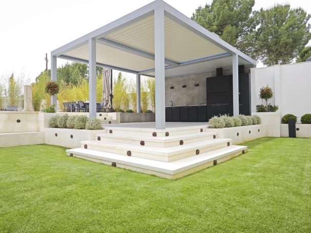 Estructura moderna con pérgola bioclimática, escalones y césped verde en un ambiente al aire libre.