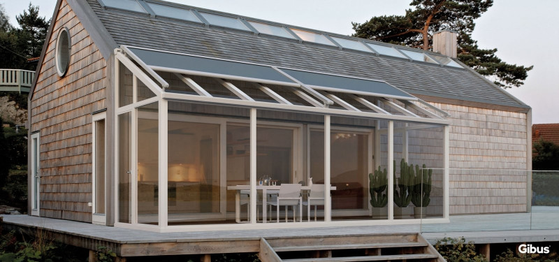 Casa moderna con gran terraza y paredes de vidrio, rodeada de naturaleza.